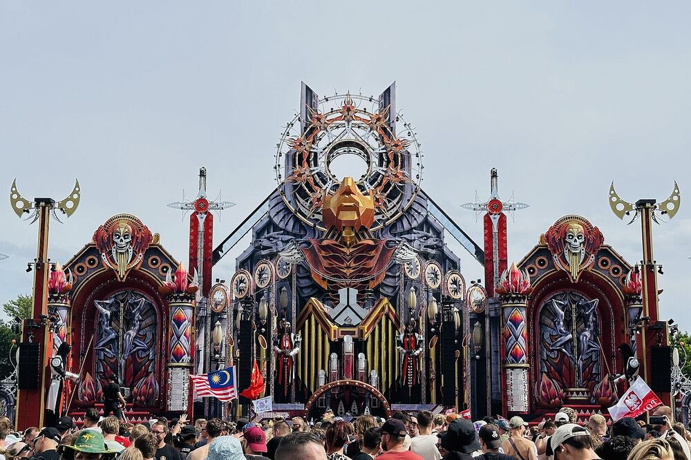 Groot rijkversierd festivalpodium met een menigte bezoekers ervoor onder een blauwe lucht